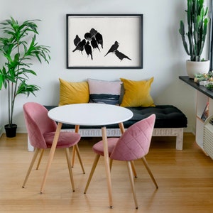May include: A white round table with a wood base and two pink velvet chairs. The table is set in a living room with a black couch, yellow and pink throw pillows, and a black and white print of birds on the wall.