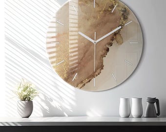 May include: A round wall clock featuring an abstract design with swirling shades of beige, brown, and metallic gold accents. The clock face has thin white hour markers and simple white hands, creating a clean look against the fluid colour pattern.
