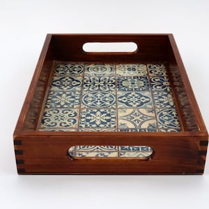 Op de afbeelding: Een rechthoekige houten dienblad met twee handvatten. Het dienblad heeft een blauw en wit patroon op de bodem.