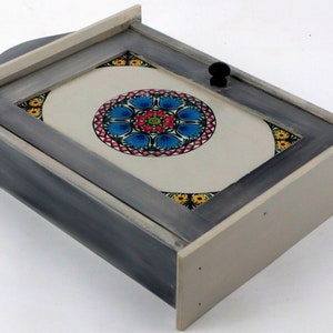 Può includere: Un porta chiavi in legno grigio con una porta bianca e un design circolare di mandala colorato sul davanti. La porta ha una maniglia nera.