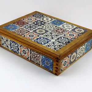 May include: A wooden box with a hinged lid. The lid and sides of the box are decorated with a colorful mosaic pattern of blue, red, and white tiles.