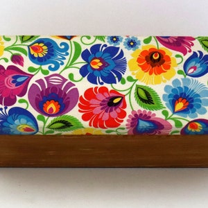 May include: A wooden box with a colourful floral pattern on the lid. The flowers are red, yellow, blue, green, and purple. The box is made of natural wood and has a simple design.