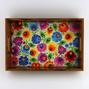 May include: A wooden serving tray with a colourful floral pattern. The tray has a brown wooden frame and two handles on the sides.