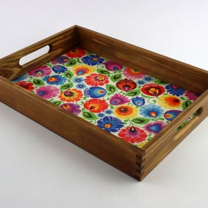 May include: A wooden serving tray with two handles. The tray is stained a dark brown colour and has a colourful floral pattern on the bottom.