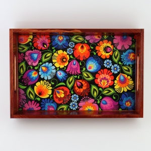 May include: Wooden serving tray with a rectangular shape and a floral design. The tray has a dark wood frame and a colourful pattern of flowers in red, orange, yellow, blue, and purple on a black background.