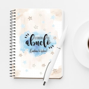 May include: A white spiral bound notebook with a blue watercolor background and stars. The notebook has the text "El Cuaderno del Abuelo" and "¡Cuéntame tu historia!" written in black.