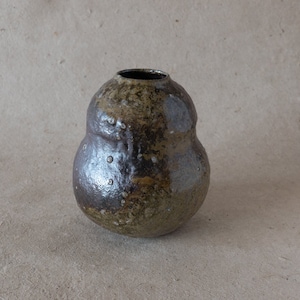 May include: A small, brown and grey ceramic vase with a rounded, pear-shaped body. The vase has a textured surface and a slightly uneven rim.