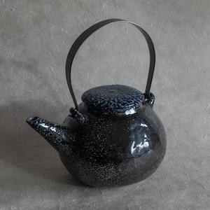 May include: A black and blue speckled teapot with a metal handle. The teapot has a round body and a lid with a speckled design.