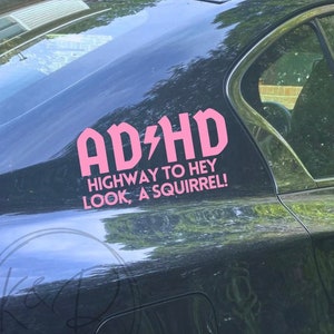 May include: A black car with a pink sticker that says "AD/HD Highway to Hey Look, A Squirrel!"