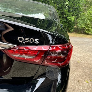 May include: A black car with the model name "Q50S" on the back. The taillights are covered with white bat decals.