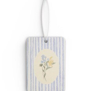 May include: Rectangular air freshener with a blue and white striped background and a floral design. The floral design features yellow and blue flowers in an oval shape. A white string is attached for hanging.