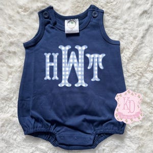 May include: A navy blue baby onesie with a white and blue gingham monogram "HWT" on the front. The onesie has a sleeveless design and a ruffled bottom.