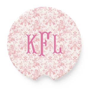 May include: Round car coaster with a floral pattern in shades of pink and white. The coaster features the pink monogram "KFL" in a serif font. The coaster has a small notch on one side.