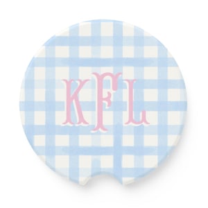 May include: A round car coaster with a light blue and white gingham pattern. The coaster features the pink monogram "KFL" in a decorative font. The coaster has a curved notch for easy removal from a car cup holder.