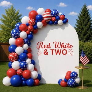 May include: A white arched backdrop featuring the red text Red White & TWO with firework graphics, decorated with a large balloon garland in red, white, and blue, including star-patterned balloons and a small American flag on a gold stand.