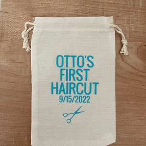May include: A white cotton drawstring bag with the text "OTTO'S FIRST HAIRCUT 9/15/2022" and a pair of blue scissors printed on it.