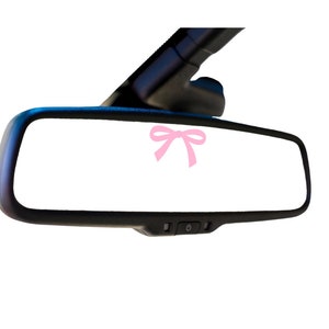 May include: A black rearview mirror with a pink bow sticker on the glass.