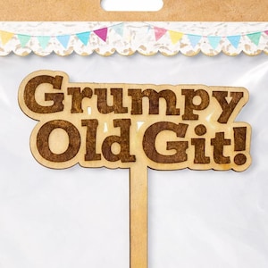 May include: A wooden cake topper with the words "Grumpy Old Git!" in a brown font. The topper is on a stick and packaged in a clear plastic bag with a brown header featuring a colourful banner design.