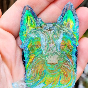 May include: A colorful, abstract dog-shaped pendant with a textured, iridescent surface. The pendant features shades of blue, green, and gold, resembling a watercolor painting. The dog's features are subtly defined, creating a unique piece of art.
