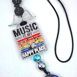 May include: A black cord with a decorative charm featuring the text "MUSIC IS MY HAPPY PLACE". The charm has a rainbow design with headphones and musical notes. The charm is connected to a black cord with decorative beads.