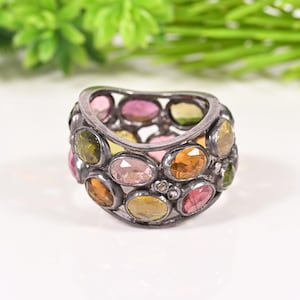 Può includere: Un anello d'argento con una serie di pietre preziose ovali nei toni del rosa, giallo, arancione e verde. Le pietre sono incastonate in una fascia aperta, creando un gioiello colorato e accattivante. Un accessorio di moda.