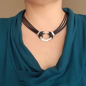 May include: A black leather choker necklace with a silver, textured, oval pendant.