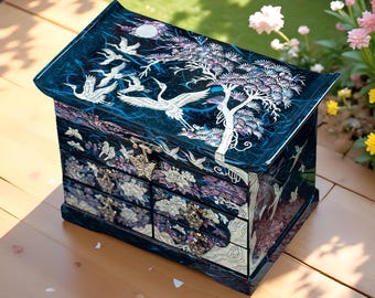 May include: A dark blue jewelry box featuring intricate mother-of-pearl inlay designs of flying cranes, a pine tree, and floral patterns. The rectangular chest has a hinged lid and four small drawers, each equipped with ornate metal pulls.