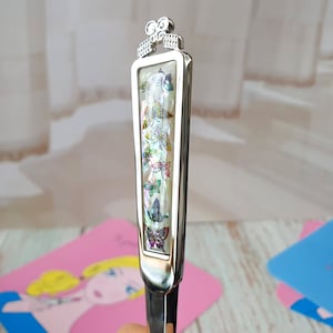 May include: A silver letter opener with a decorative handle featuring a row of colorful butterflies. The handle is made of mother of pearl and has a silver bow at the top.