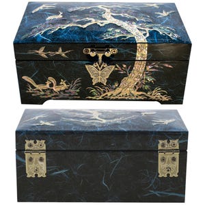K&ouml;nnte beinhalten: Zwei schwarze dekorative Boxen mit aufwendigen Perlmutt-Inlays. Die obere Box zeigt ein Baum- und Vogeldesign, w&auml;hrend die untere Box Messingbeschl&auml;ge hat. Die Boxen sind rechteckig und haben einen dunkelblauen Hintergrund.