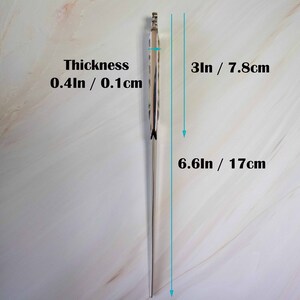May include: A silver metal knitting needle with a pointed tip. The needle is 6.6 inches long and 0.4 inches thick. The needle is shown against a white background.