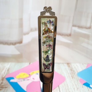 May include: A silver butter knife with a decorative handle featuring a white background with colorful butterfly designs.