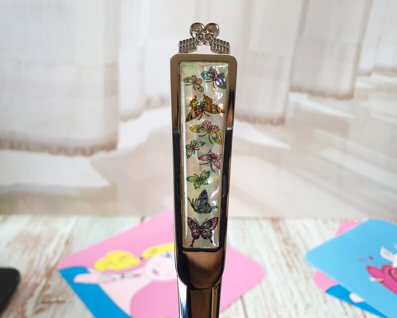 May include: A silver butter knife with a decorative handle featuring a white background with colorful butterfly designs.