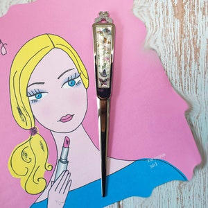 May include: A silver letter opener with a butterfly design and a pink and blue background. The text "I'm Vogue Girl" is written on the background.