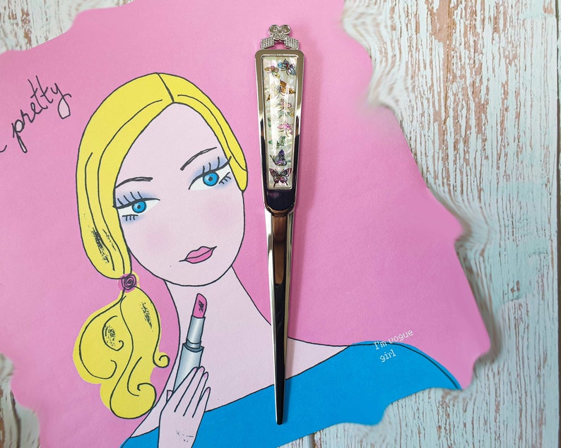 May include: A silver letter opener with a butterfly design and a pink and blue background. The text "I'm Vogue Girl" is written on the background.