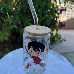 May include: A clear glass Harry Potter themed tumbler with a bamboo lid and a glass straw. The tumbler features a cartoon image of Harry Potter flying on a broomstick with the words "Harry Potter" on the side.