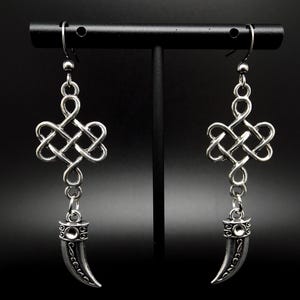Può includere: Orecchini pendenti in argento con un design a nodo e un ciondolo a forma di zanna.