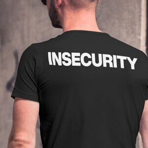 Op de afbeelding: Een zwart T-shirt met het woord "INSECURITY" in wit op de rug.