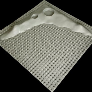 May include: A gray plastic base plate with a raised gray plastic boomerang shape. The base plate has a grid of small circles.