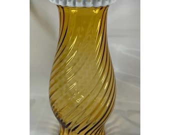 Pode incluir: Um vaso de vidro alto na cor âmbar com um padrão distinto de nervuras em espiral por todo o corpo. O vaso tem uma abertura larga e alargada, finalizada com uma borda decorativa de vidro branco recortado que contrasta com os tons dourados.