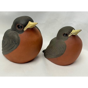 May include: Two bird figurines with dark gray heads and wings, featuring rounded terracotta-colored chests and small, pointed yellow beaks. Each bird has a smooth, matte finish and dark, glossy eyes, presented as a pair of varying sizes.