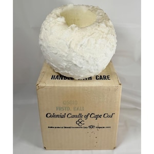 May include: A white, textured, spherical candle resting on a cardboard box. The box features the text "HANDLE WITH CARE", "Q6810 FRSTD. BALL", and "Colonial Candle of Cape Cod" with the company logo and "Another product of General Housewares Corp."