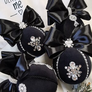 Puede incluir: Cuatro adornos navide&ntilde;os de terciopelo negro con adornos plateados y lazos de sat&eacute;n negro. Los adornos est&aacute;n decorados con diamantes de imitaci&oacute;n y tienen un borde plateado. El texto "DEKOR BY ME" es visible en el fondo.