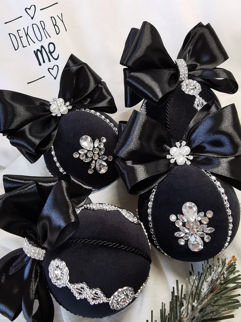 Puede incluir: Cuatro adornos navide&ntilde;os de terciopelo negro con adornos plateados y lazos de sat&eacute;n negro. Los adornos est&aacute;n decorados con diamantes de imitaci&oacute;n y tienen un borde plateado. El texto "DEKOR BY ME" es visible en el fondo.