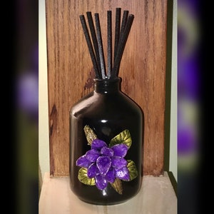 May include: Black glass diffuser bottle with a purple flower design and black diffuser sticks.