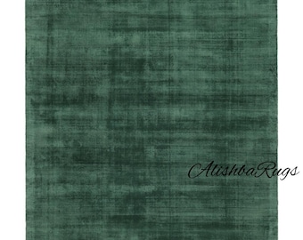 May include: A rectangular, emerald green rug with a textured surface. The rug has a subtle, distressed appearance, with variations in the green hue. The text "Alishba Rugs" is in the bottom right corner. This rug is suitable for living rooms and bedrooms.