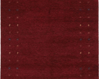 May include: A rectangular, deep red rug with a textured surface. The rug features a border of small, repeating geometric patterns in gold and navy blue. The central field is a solid, rich red.