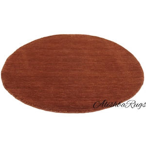 May include: A round, rust-colored rug with a textured surface. The rug is a solid color and has a simple, minimalist design. The rug is suitable for a living room or bedroom.