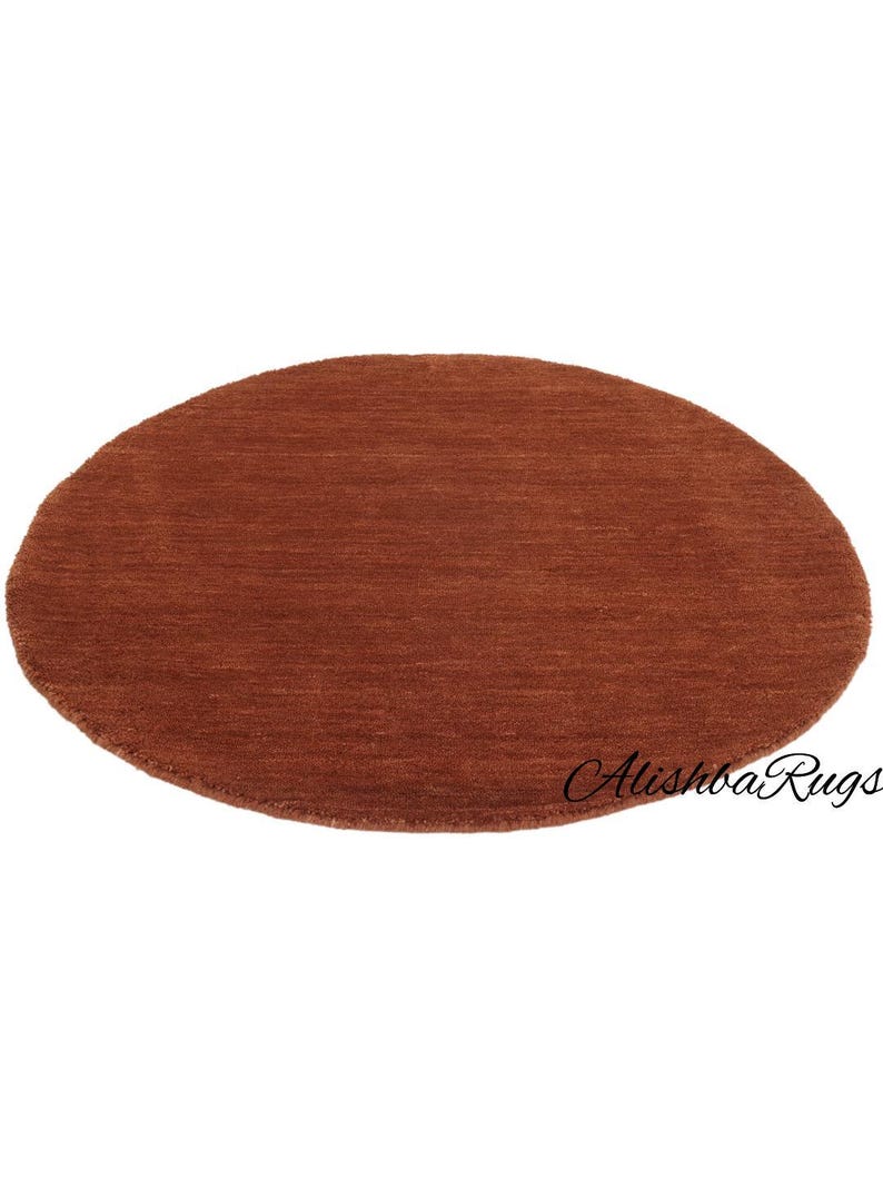 May include: A round, rust-colored rug with a textured surface. The rug is a solid color and has a simple, minimalist design. The rug is suitable for a living room or bedroom.