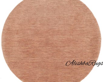 May include: A round, light brown rug with a textured surface. The rug has a simple design and is suitable for various interior styles. The text "Alishba Rugs" is written in cursive on the rug.