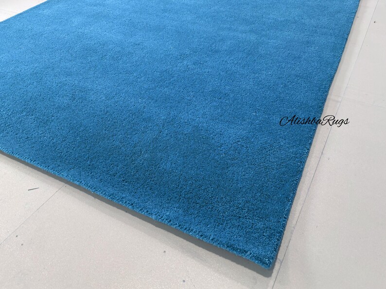 May include: A rectangular, solid blue rug with a soft, textured surface. The rug is a vibrant shade of turquoise and is placed on a light-colored surface. The text "Atishba Rugs" is visible in the image.